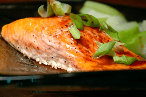 cooked steelhead trout fillet on plate with spring onion