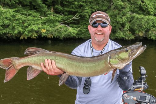 man holding muskie fish caught on boat