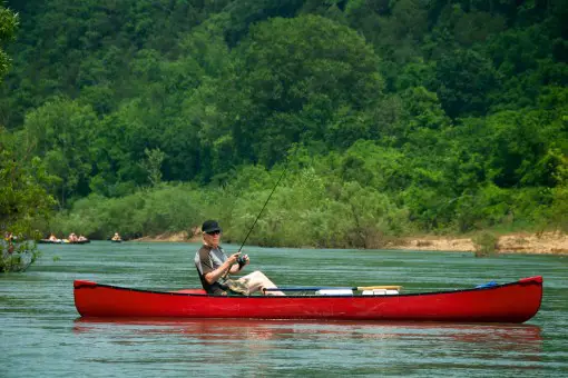 man fishing on a river from a canoe