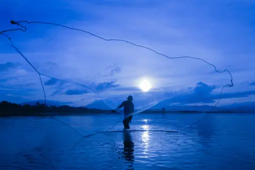 man throwing a fishing net a night