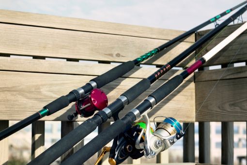 three fishing rods with reels resting on a fence
