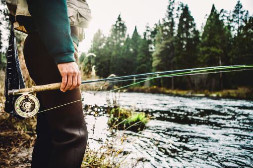 fly fisherman holding fly rod beside a river