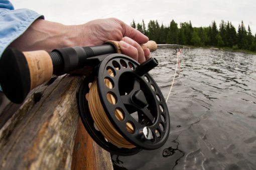 close up of a fly fishing rod and reel in hands of fishermen