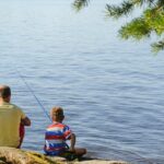 father and son fishing a lake from the shore