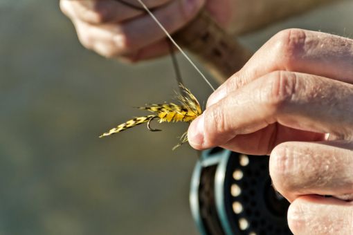 two hands tying a fly fishing fly to line