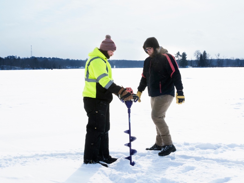 two men drilling ice fishing hole with auger